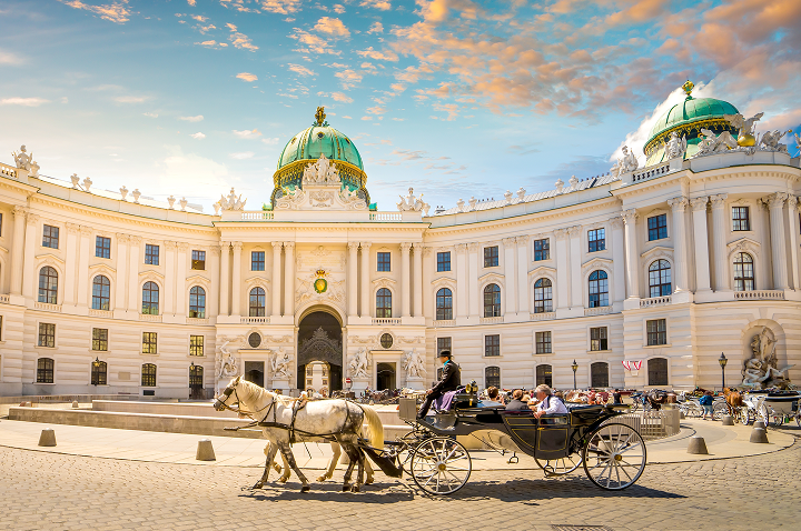 Eine Kutsche mit Pferden ist vor einem Wiener Gebäude abgestellt.